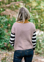 Back view of Blonde model wearing a sweater with a taupe bodice and black and white striped sleeves.