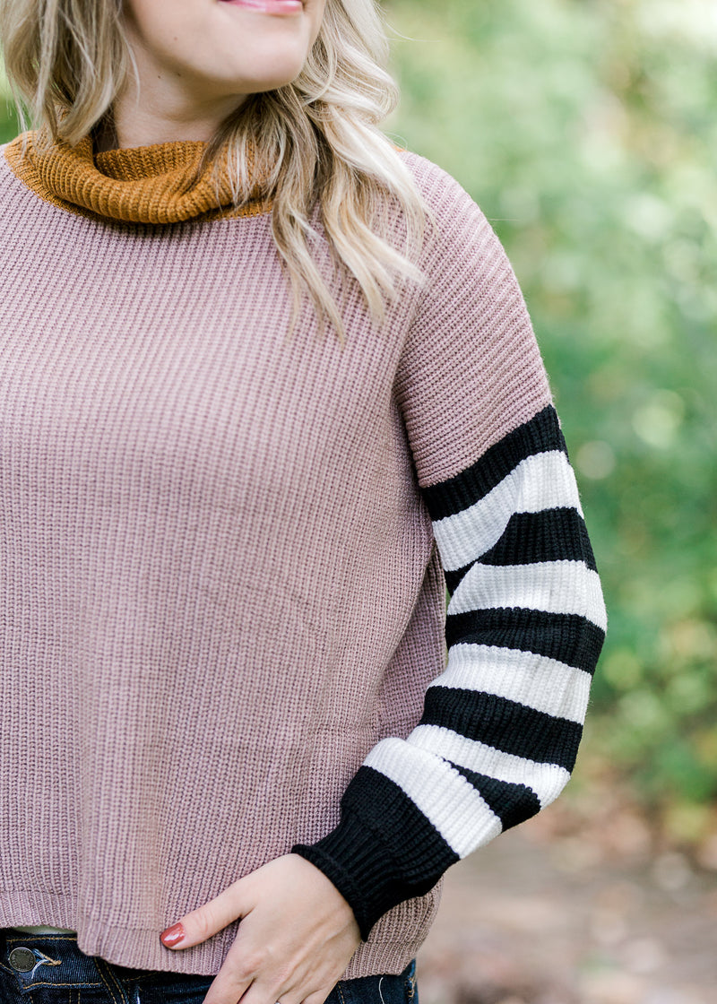 Close up view of a sweater with a taupe bodice and black and white striped sleeves.