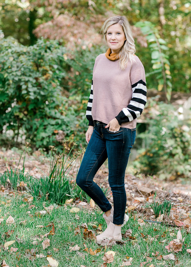 Blonde model wearing jeans and a taupe sweater with black and white striped sleeves.