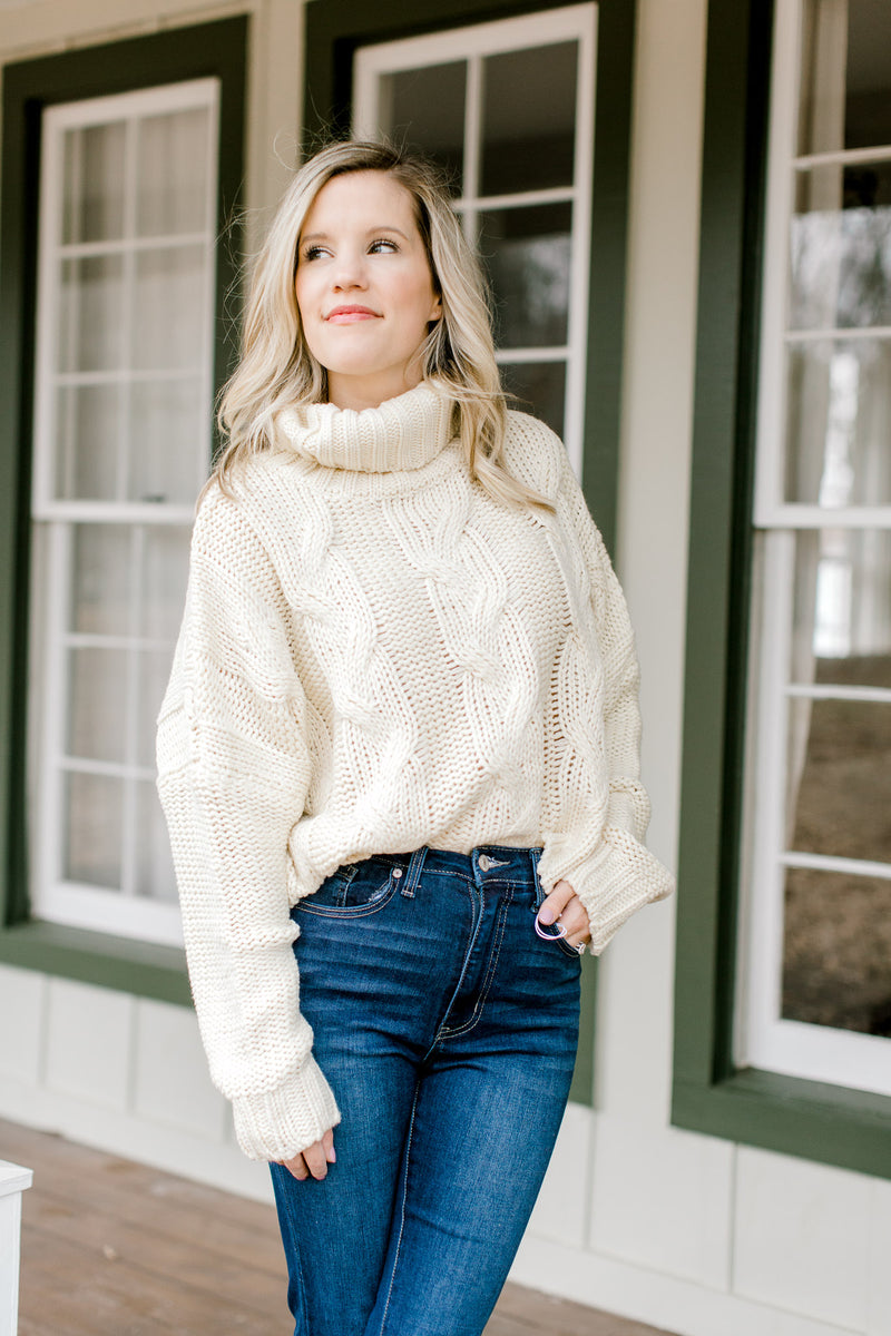 Blonde model wearing a cable knit ivory sweater with a turtleneck.