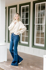 Blonde model wearing a cable knit ivory sweater with wide leg jeans.