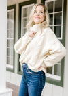 Blonde model wearing a cable knit ivory sweater tucked into jeans.  