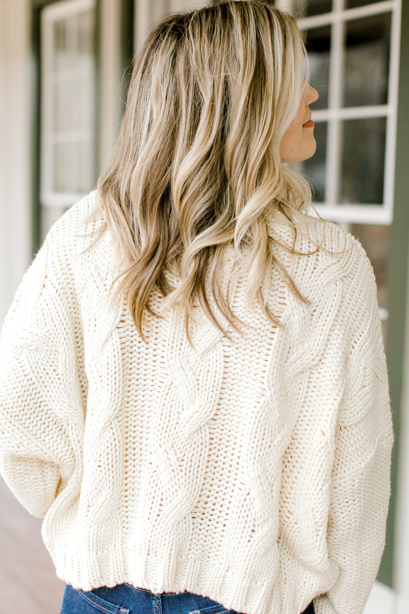 Back view of Blonde model wearing a cable knit ivory sweater.