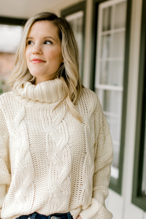 Blonde model wearing a cable knit ivory sweater. 