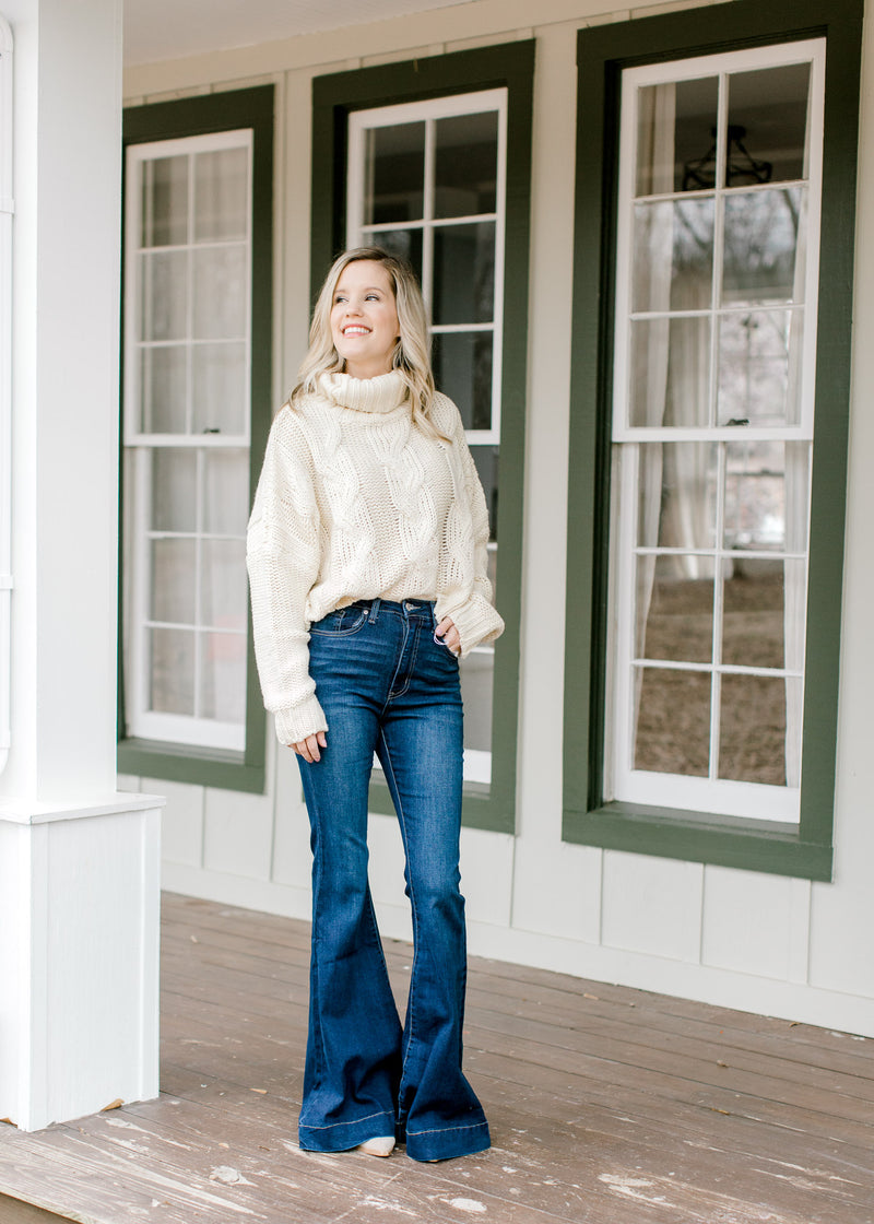Blonde model wearing a cable knit ivory sweater with wide leg jeans and mules. 