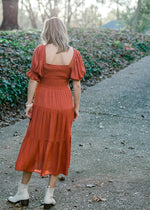 Back view of  Blonde model wearing rust colored smocked dress.