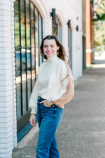 Brunette model wearing sweater with ivory front and Carmel back with jeans.