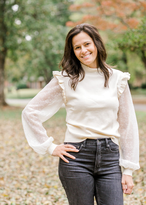 Brunette model wearing ivory colored sweater with lacework sleeves.