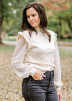 Brunette model wearing ivory colored sweater with lacework sleeves and jeans.
