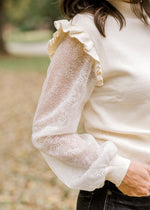 Sleeve detail of Brunette model wearing ivory colored sweater with lacework sleeves.