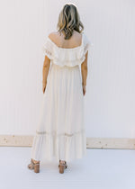 Back view of Model wearing a cream dress with lace detail, a tie at the neck and an elastic waist. 
