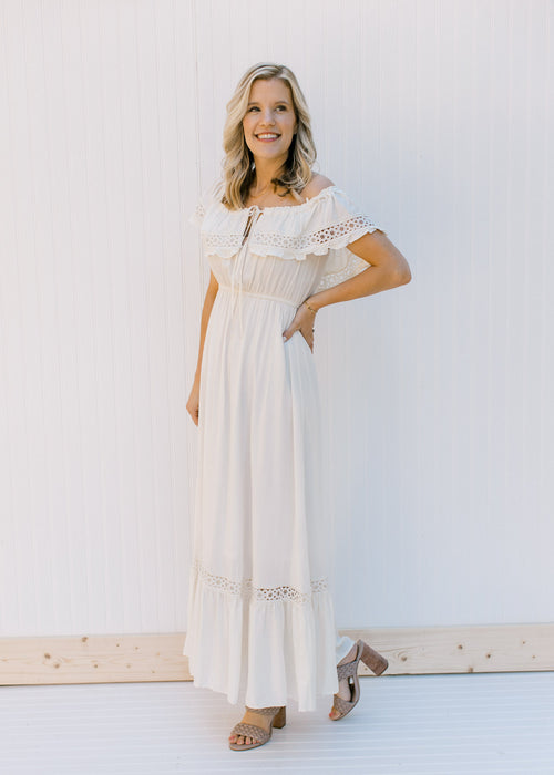 Model wearing heels and a cream dress with lace detail, a tie at the neck and an elastic waistband. 