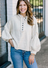 Brunette model wearing an ivory sweater with buttons.
