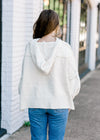 Back view of hoodie on Brunette model wearing an ivory sweater.