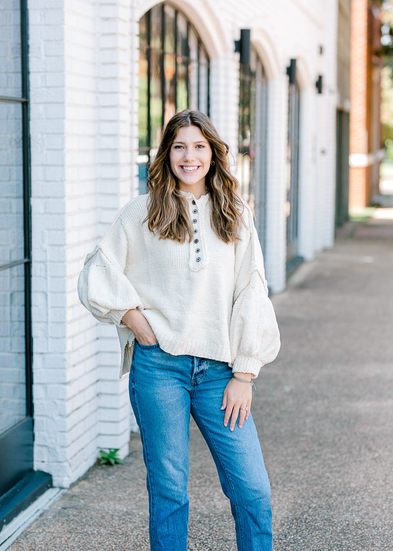 Brunette model wearing an ivory sweater with jeans.