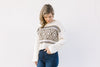 Blonde model wearing a cream Nordic sweater with a crop hem and jeans.