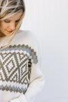 Close up view of Blonde model wearing a cream sweater with a crop hem.