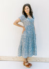 Model wearing a blue button up midi dress with an ivory floral pattern and a tiered design. 