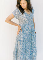 Close up view of ivory floral pattern on a blue tiered dress with a v-neck.
