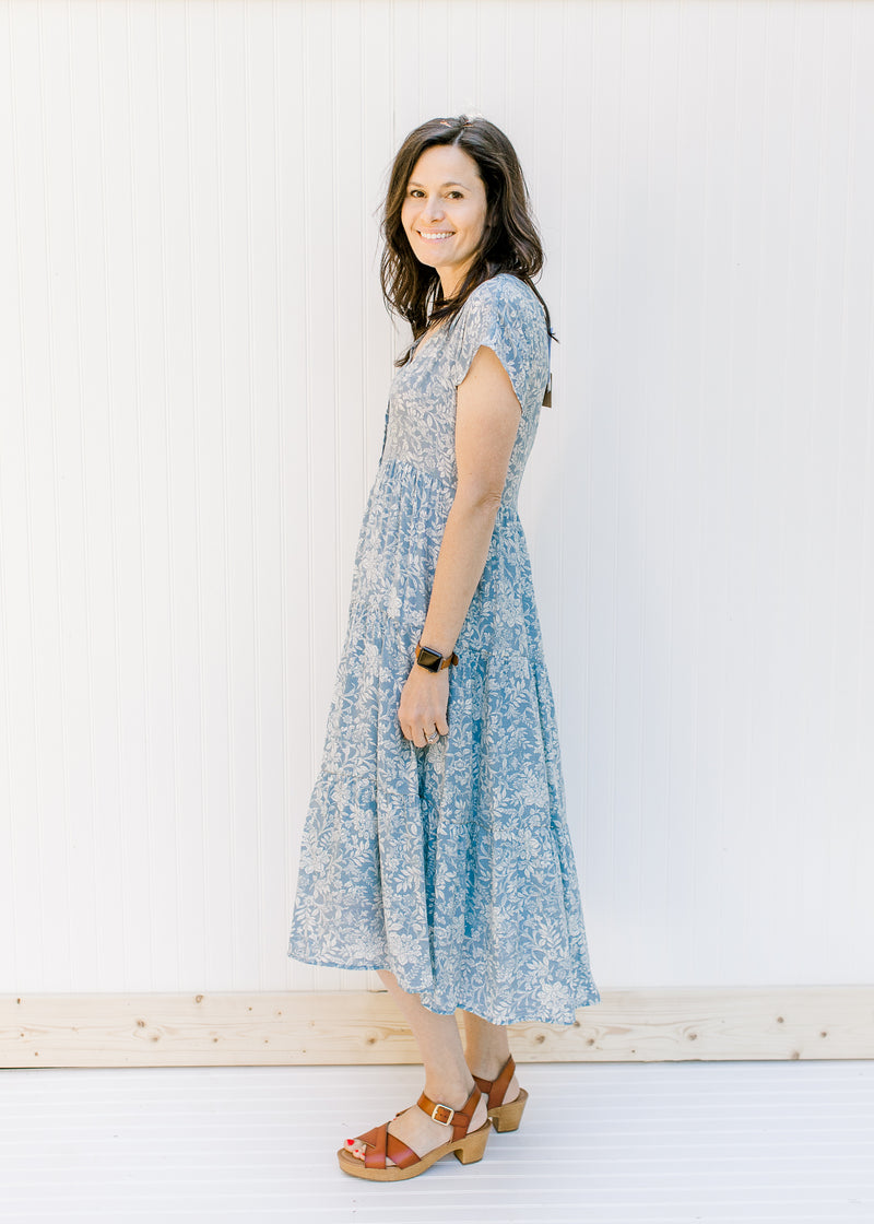 Model wearing a button up, blue, midi dress with an ivory floral pattern and brown heels. 
