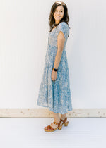 Model wearing a short sleeve, button up, blue midi dress with an ivory pattern and a tiered design. 