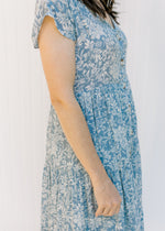 Close up view of tiers and buttons on a short sleeve, blue dress with ivory floral pattern. 