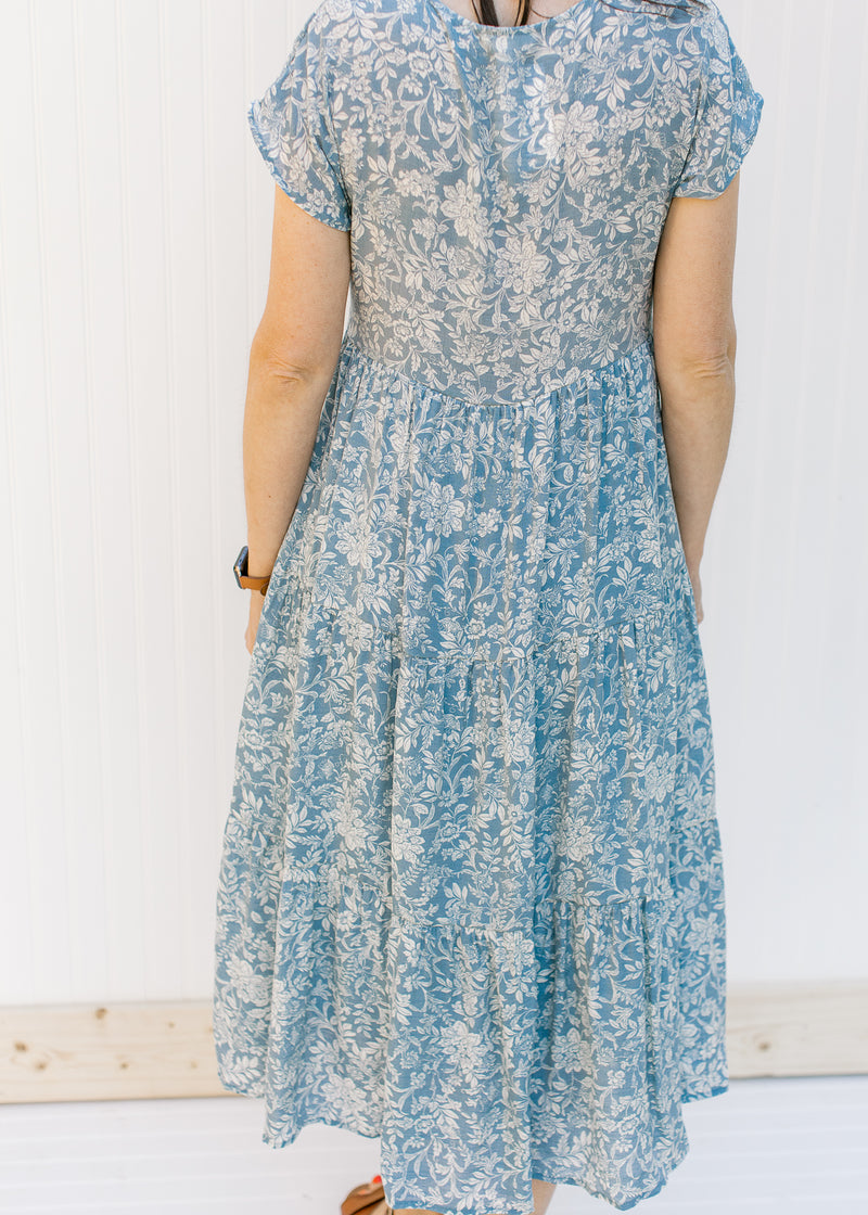 Back view of Model wearing a blue button up midi dress with an ivory pattern and a tiered design. 