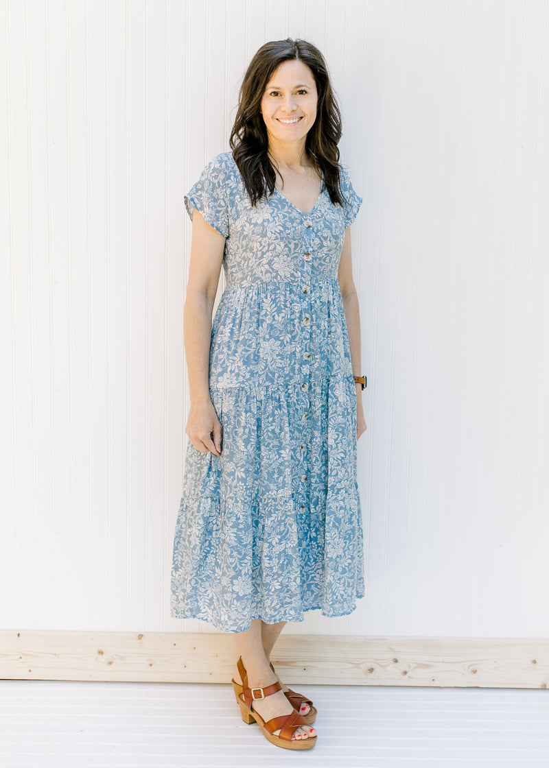Model wearing a tiered blue button up midi dress with an ivory pattern and heeled sandals. 