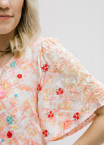 Close up view of embroidered pattern on cream top with an abstract print.