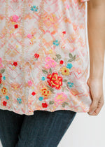 Close up view of embroidered pattern along the bottom of a cream top with abstract print.