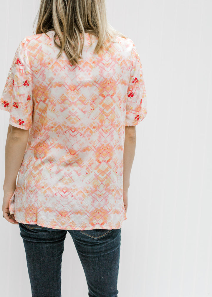 Back view of Blonde model wearing a cream top with an abstract print.