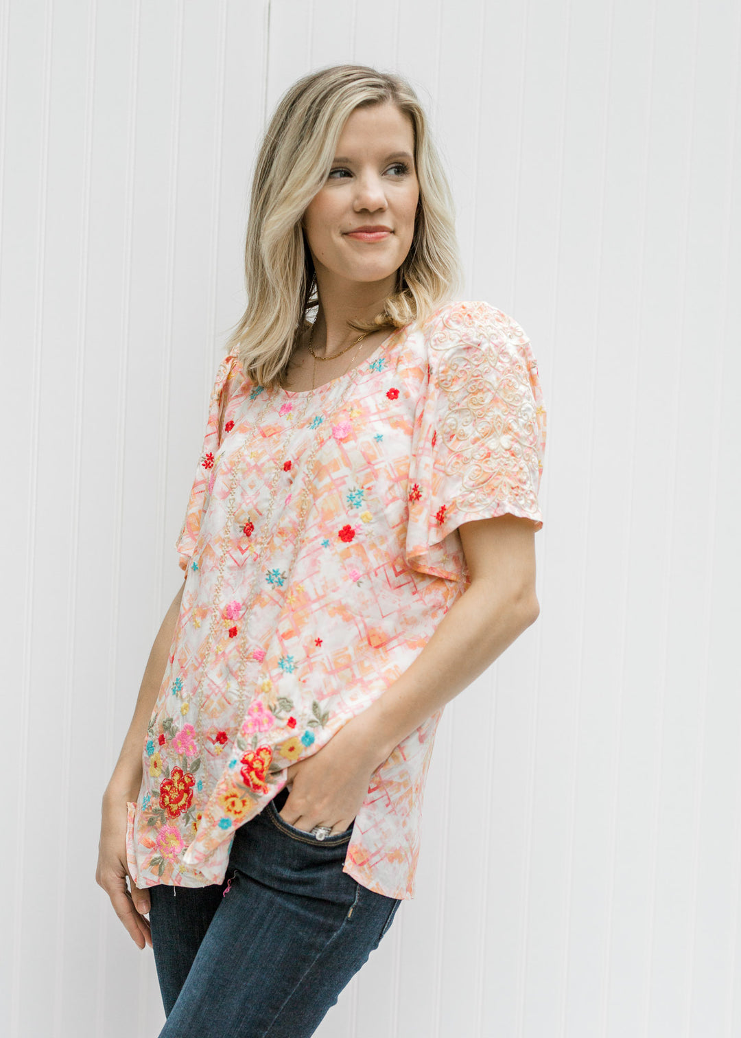 Blonde model wearing a cream top with an abstract print. 