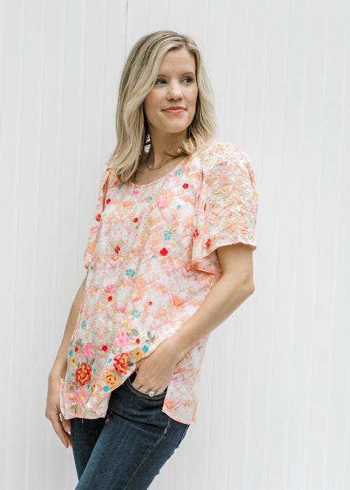 Blonde model wearing a cream top with an abstract print. 
