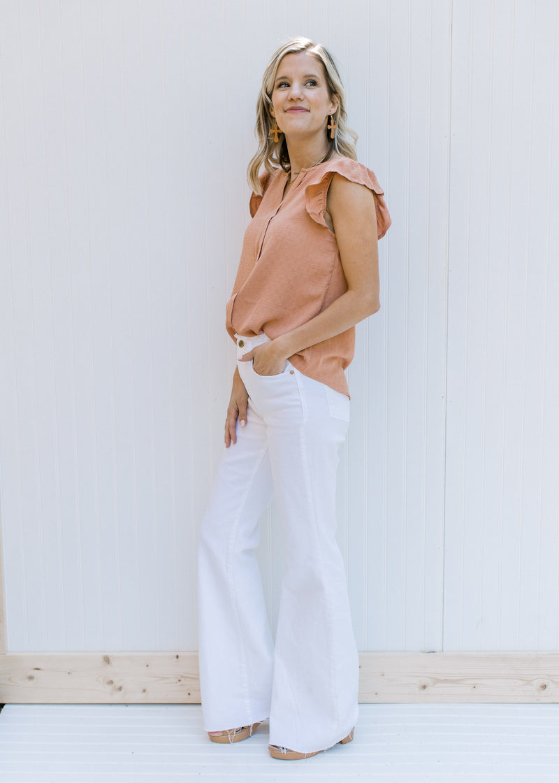 Side view of Model wearing high waisted white denim flare jeans with a frayed waist and raw hem.