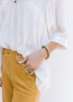 Close up of button on front pocket of marigold color crop jeans. 