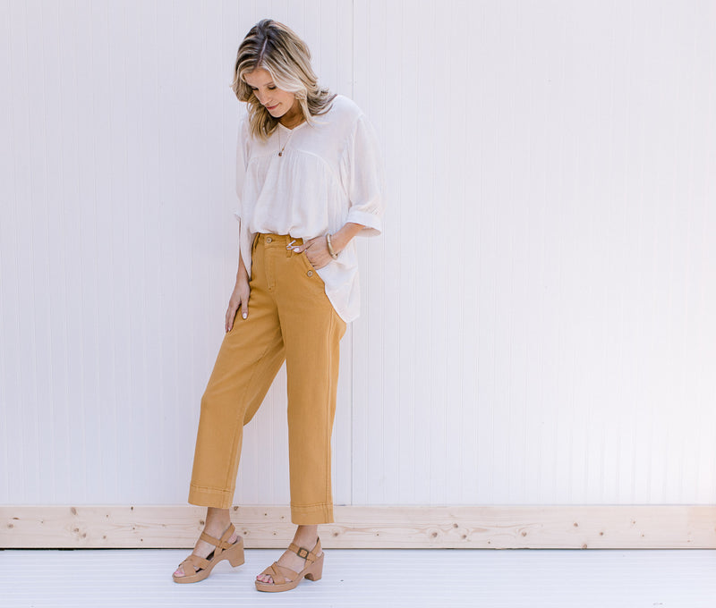 Model wearing marigold wide leg cropped jeans with a white top and heels. 