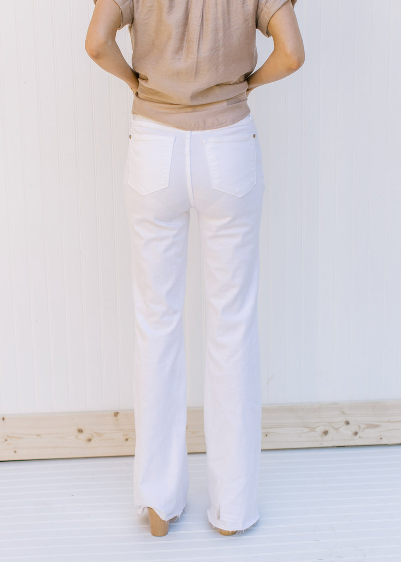 Back view of Model wearing high waisted white denim flare jeans with a frayed waist and raw hem.