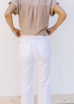 Close up view of the back of high waist, white denim flare jeans with a frayed waist and raw hem. 