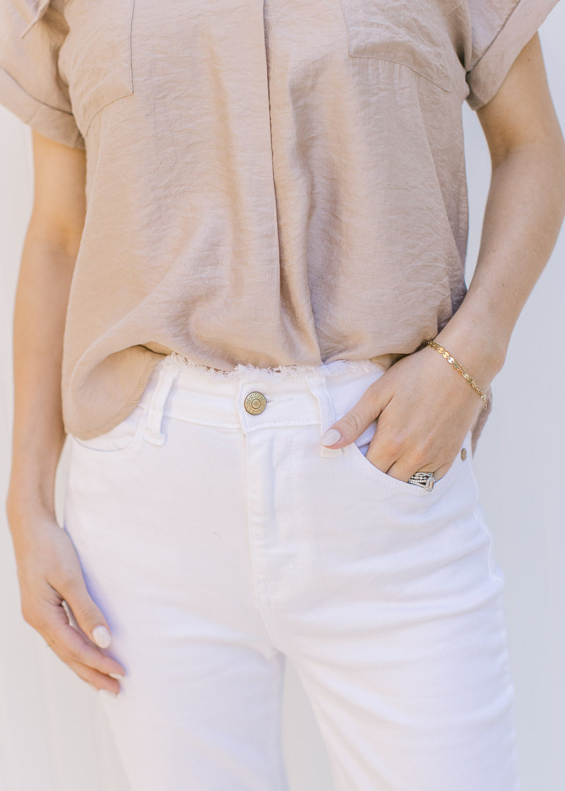 Close up of button on Model wearing hi-waisted white denim flare jeans with a frayed waist.