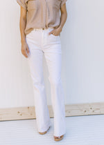 Model wearing high waisted white denim flare jeans with a frayed waist and raw hem. 