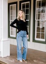 Model wearing light wash, wide leg jeans with a black top. 
