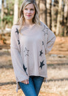 Blonde model wearing a taupe sweater with black stars.