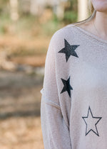 Shoulder detail of Blonde model wearing a taupe sweater with black stars.