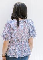 Back view of Model wearing a white top with a lavender floral pattern and bubble short sleeves.