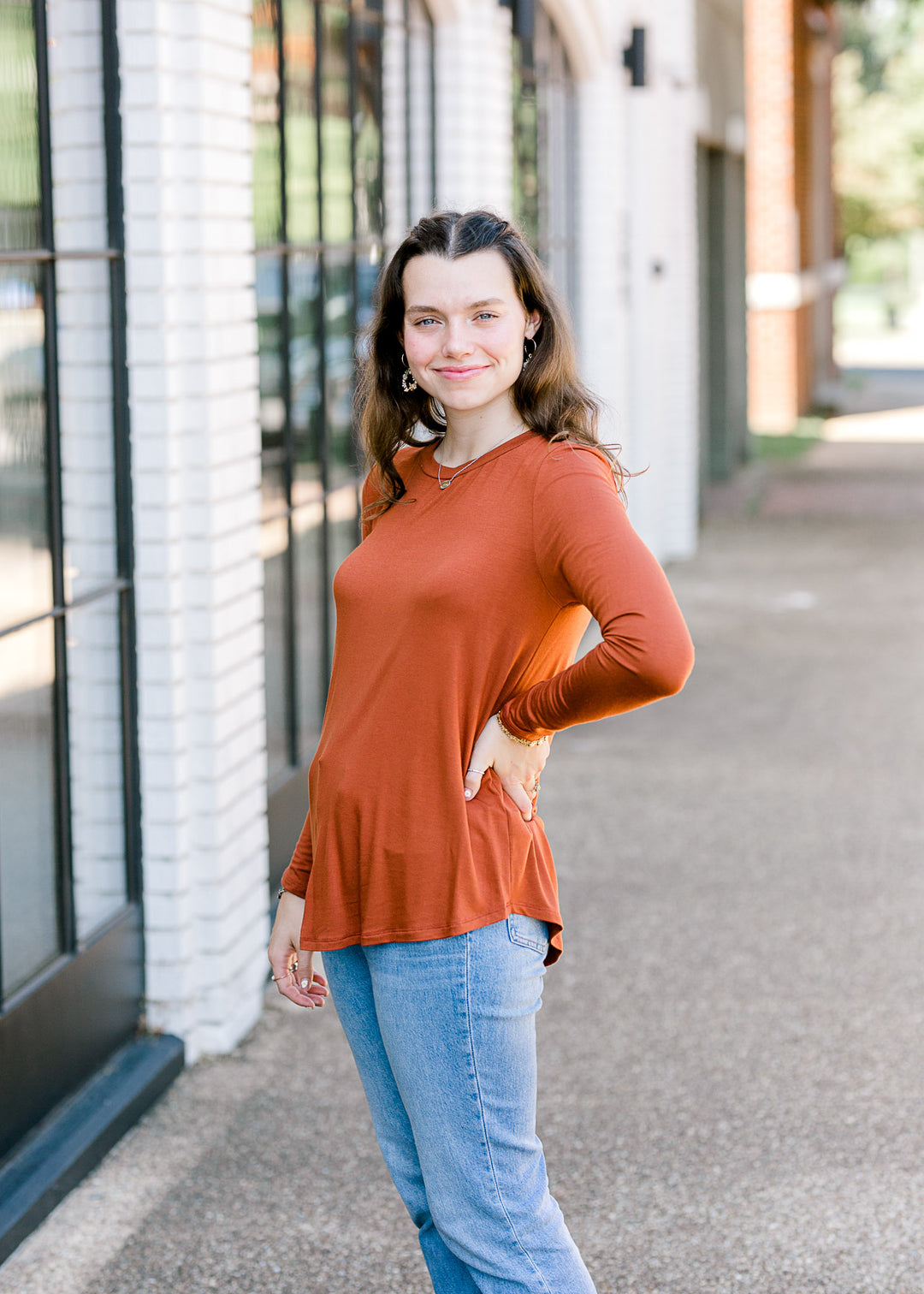 Brunette model wearing deep mauve long sleeve top with jeans.