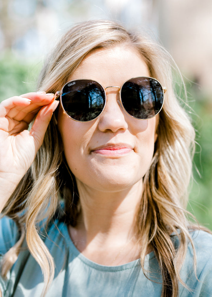 Blonde model wearing gold rimmed sunglasses. 