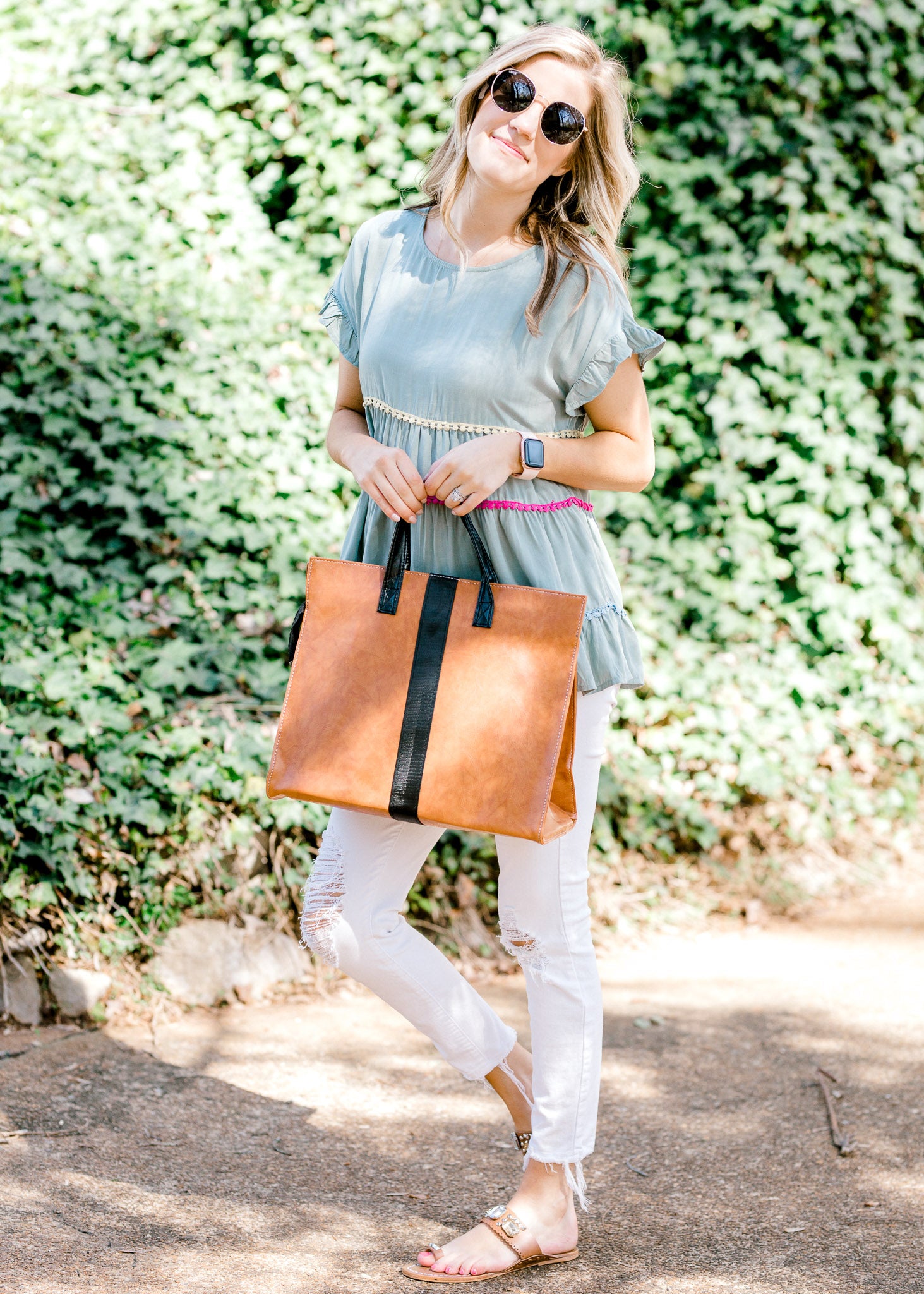 Blonde model wearing gold rimmed sunglasses while holding a bag. 