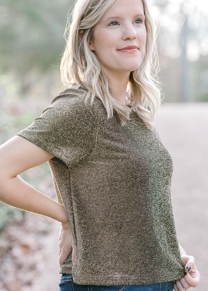 Blonde model wearing black and gold top with short sleeves.