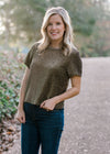 Blonde model wearing black and gold top with round neck.