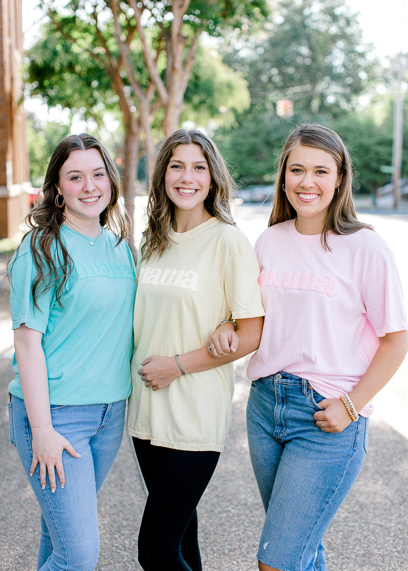 Brunette models wearing teal, yellow and pink Mama comfort color tee shirts.